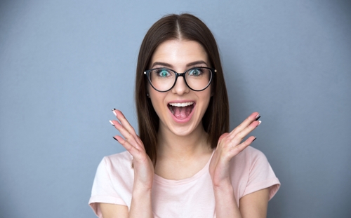 Surprised young woman in glasses over gray background